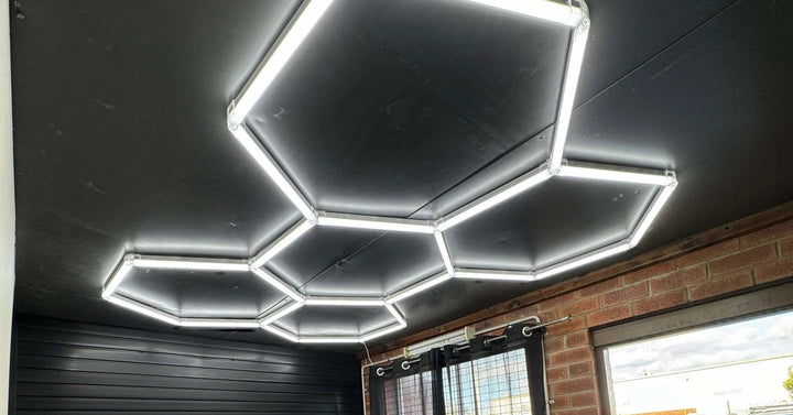 Five hexagon lights on a black ceiling beside a brick wall and window
