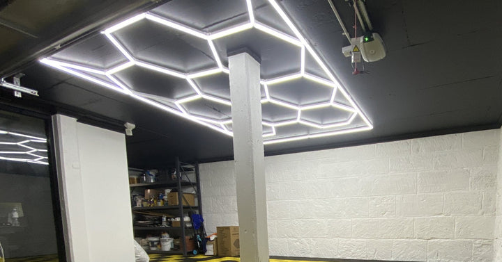 Hexagon light grid system on a black garage ceiling above white brick walls and shelving