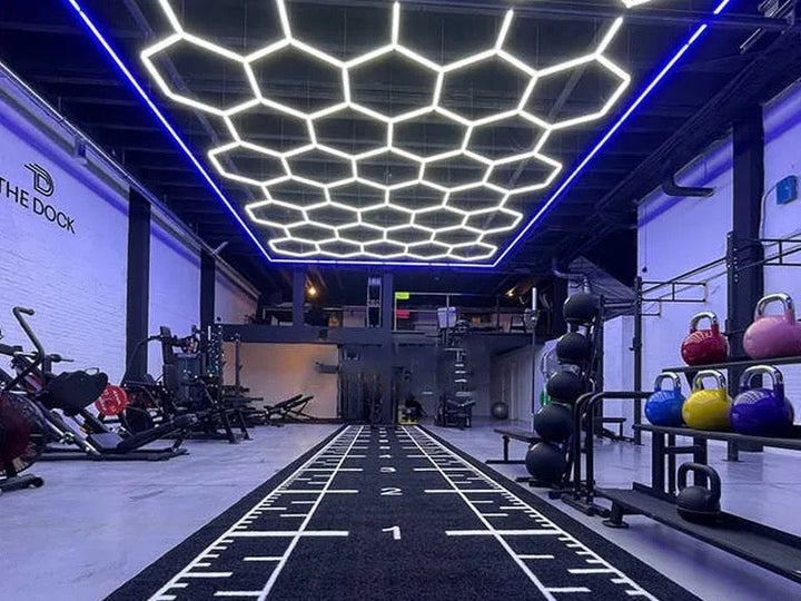Commercial gym with a large HexSpace hexagon LED lighting grid at 6500K daylight over a sprint track, kettlebells and cardio equipment